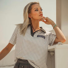 Load image into Gallery viewer, Woman wearing a polka dot shirt with a brand logo, standing against a neutral background.