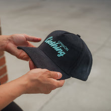 Load image into Gallery viewer, Person holding a black cap with 'Devotion Clothing' branding.