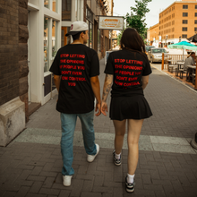 Load image into Gallery viewer, Two people walking down a street holding hands, wearing matching black t-shirts with red text.