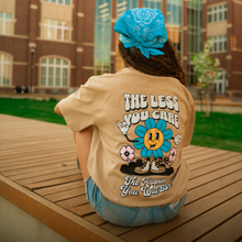 Load image into Gallery viewer, Person wearing a beige t-shirt with a colorful graphic and text, sitting on a wooden bench outdoors.