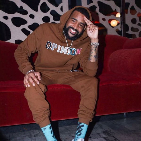 Man wearing a brown hoodie with 'OPINION' text, sitting on a red couch.
