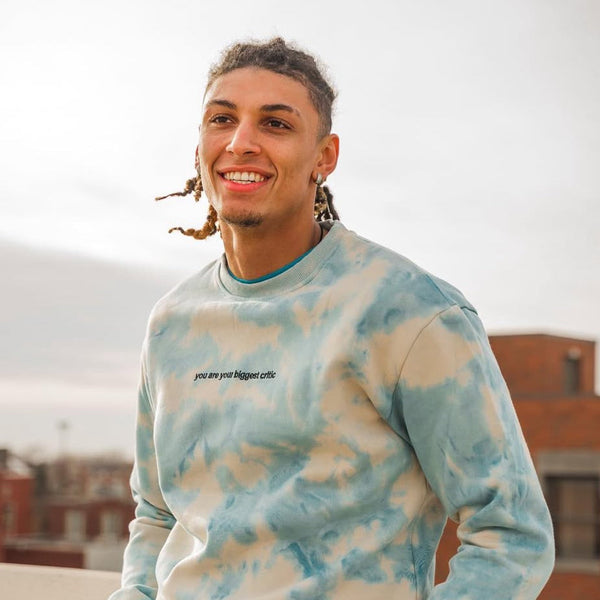Man wearing a tie-dye sweatshirt with text, standing outdoors on a cloudy day.